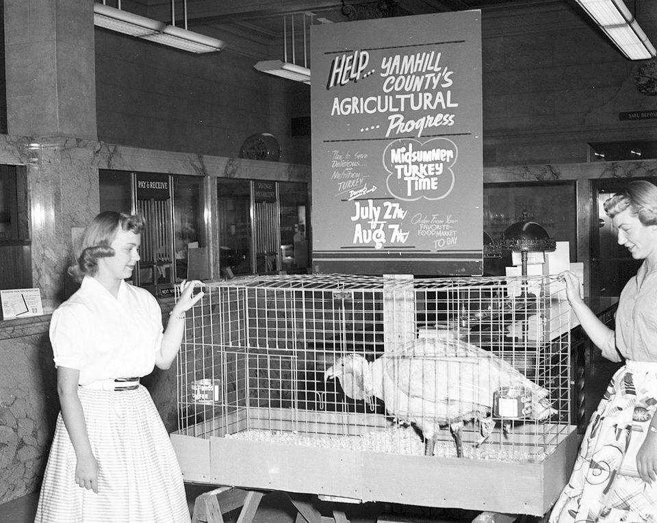 2 women by a turkey in a cage.